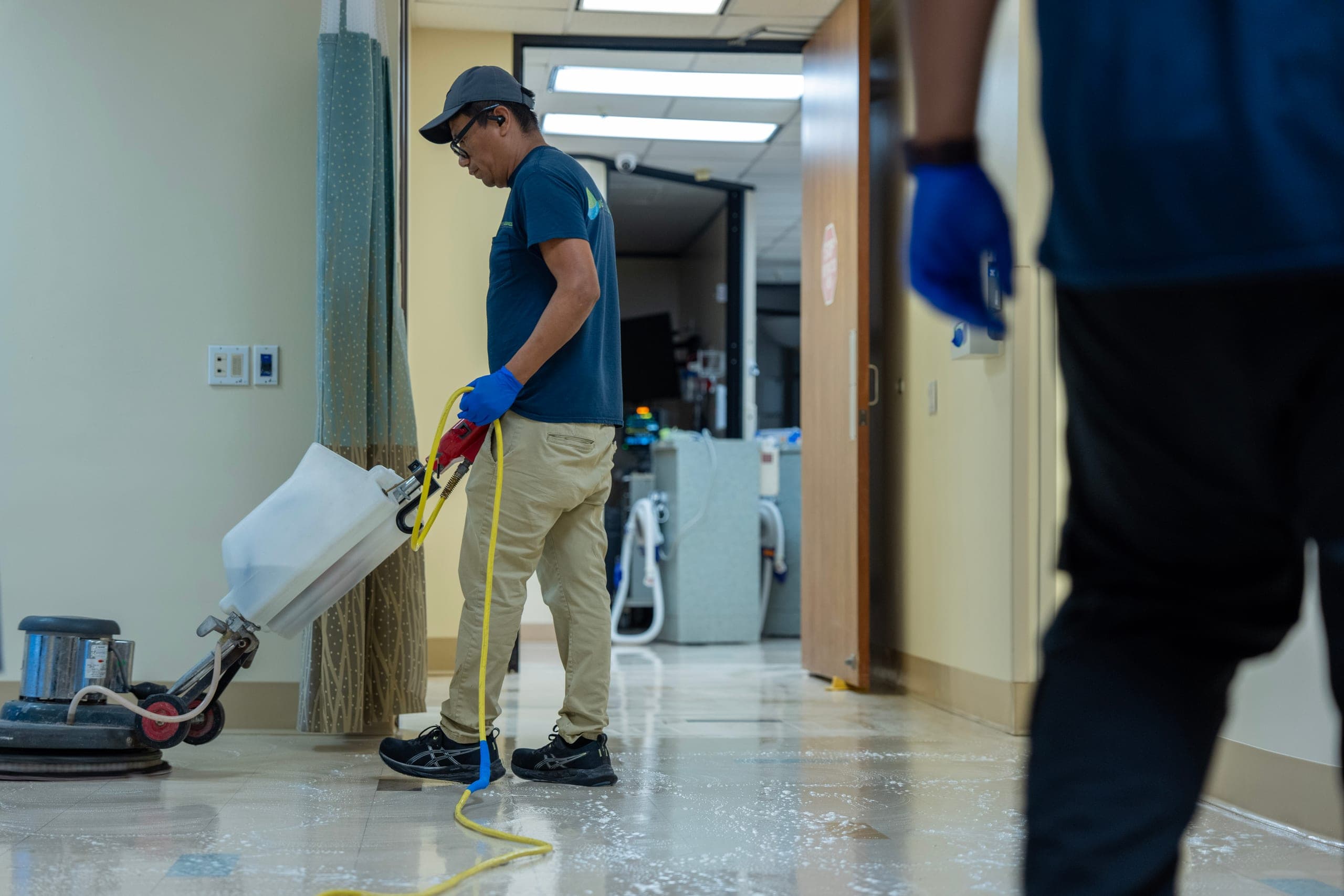 An MGS technician running a floor machine in a medical facility corridor